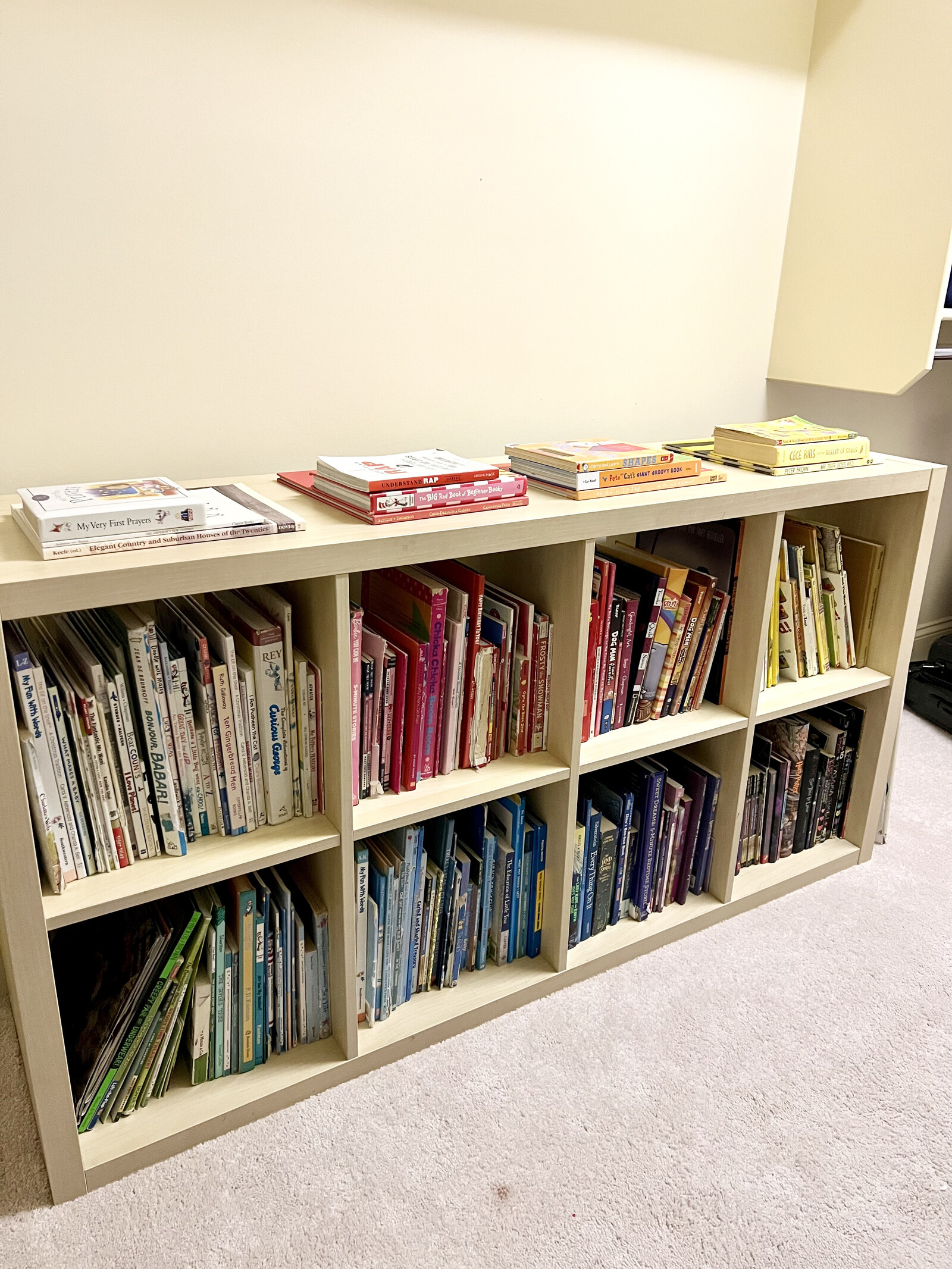 Books organized by color on a low white bookshelf