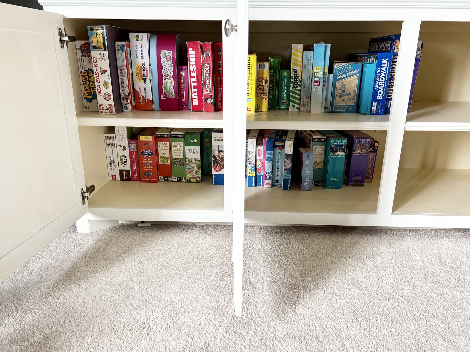 Board games and puzzles organized by color in a white cabinet